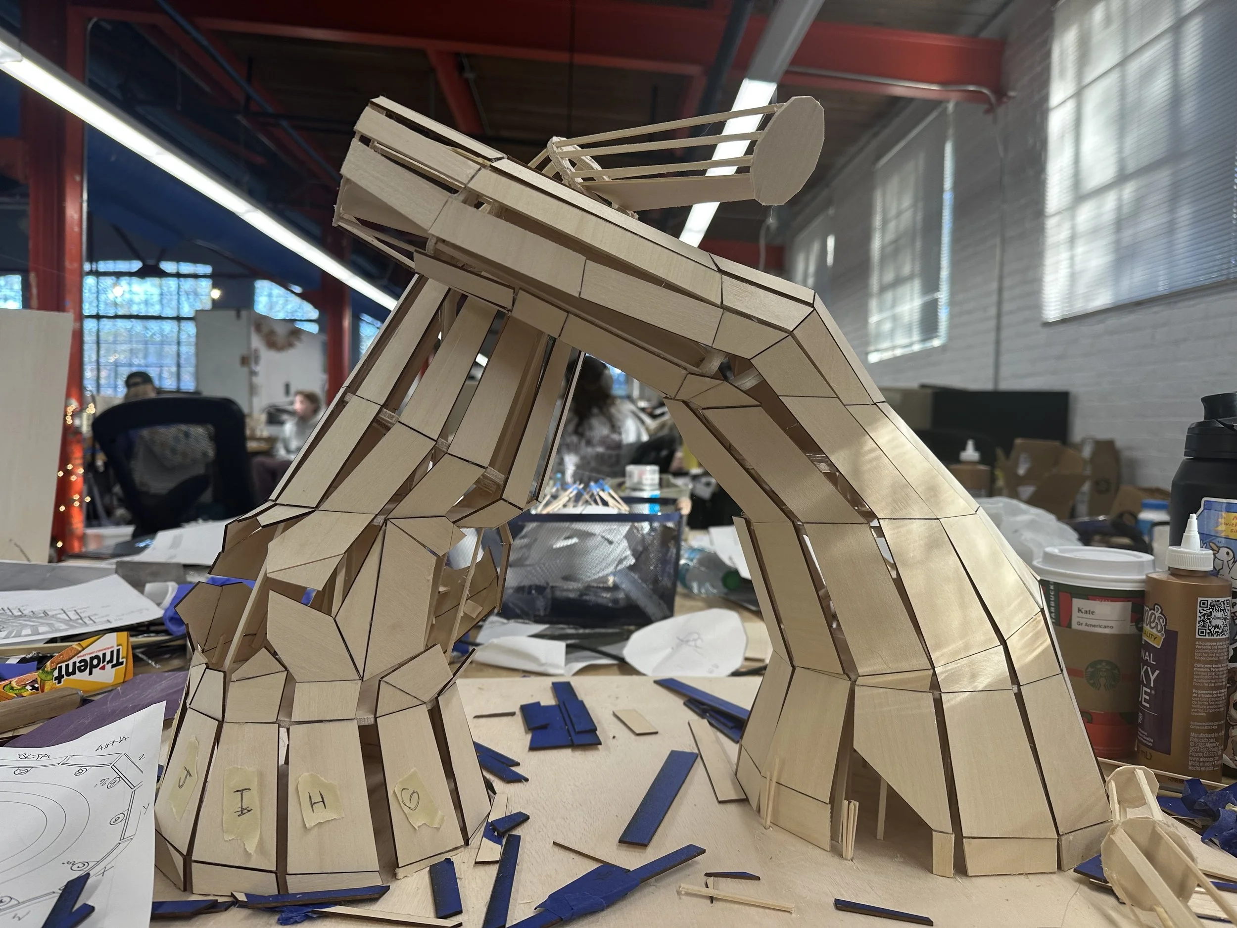 Wooden model of a giraffe under construction in a workshop with various tools and papers scattered around.