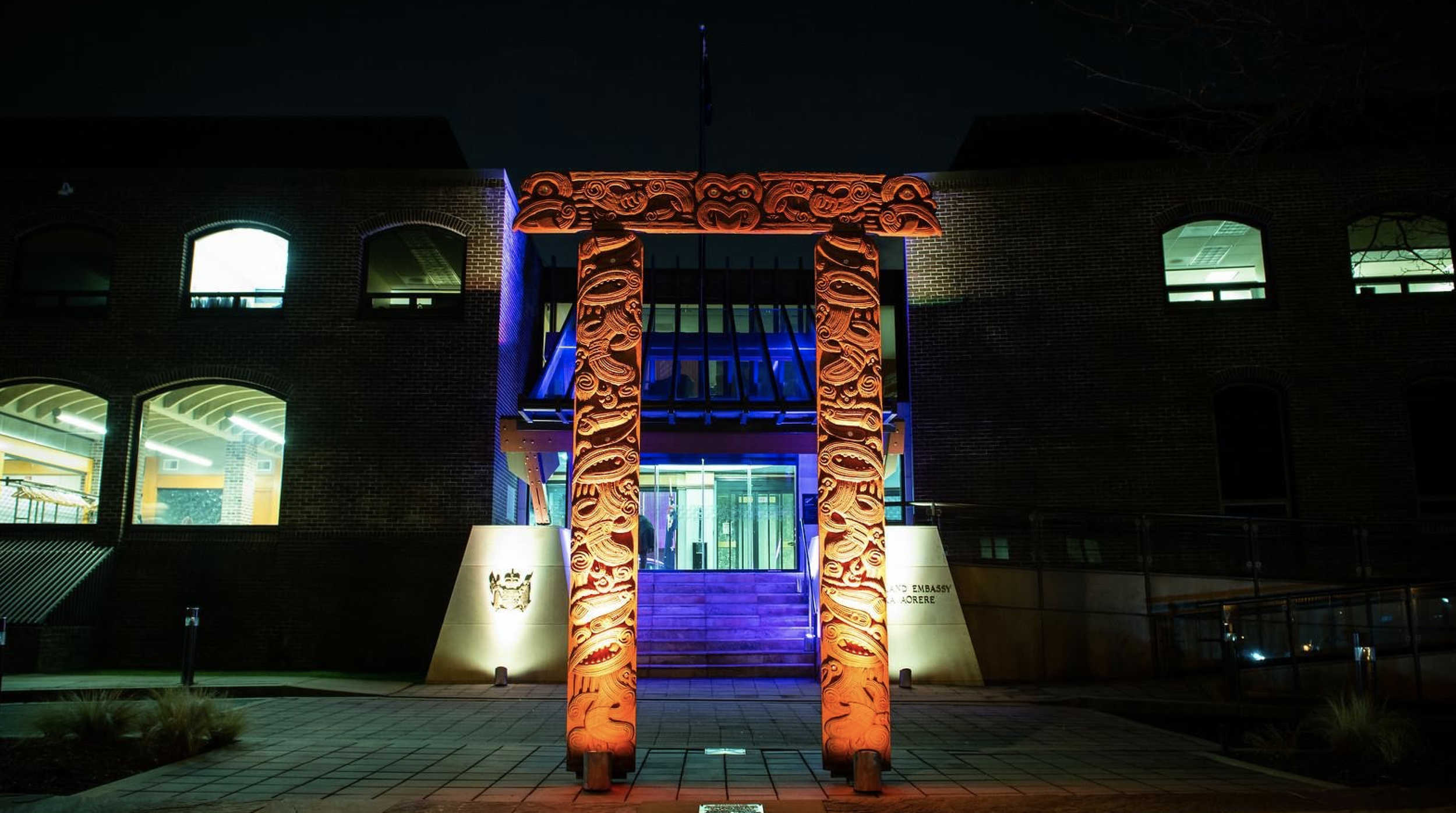 Night view of a building with illuminated Maori carvings and a flag at the top, featuring brightly lit windows and entrance.