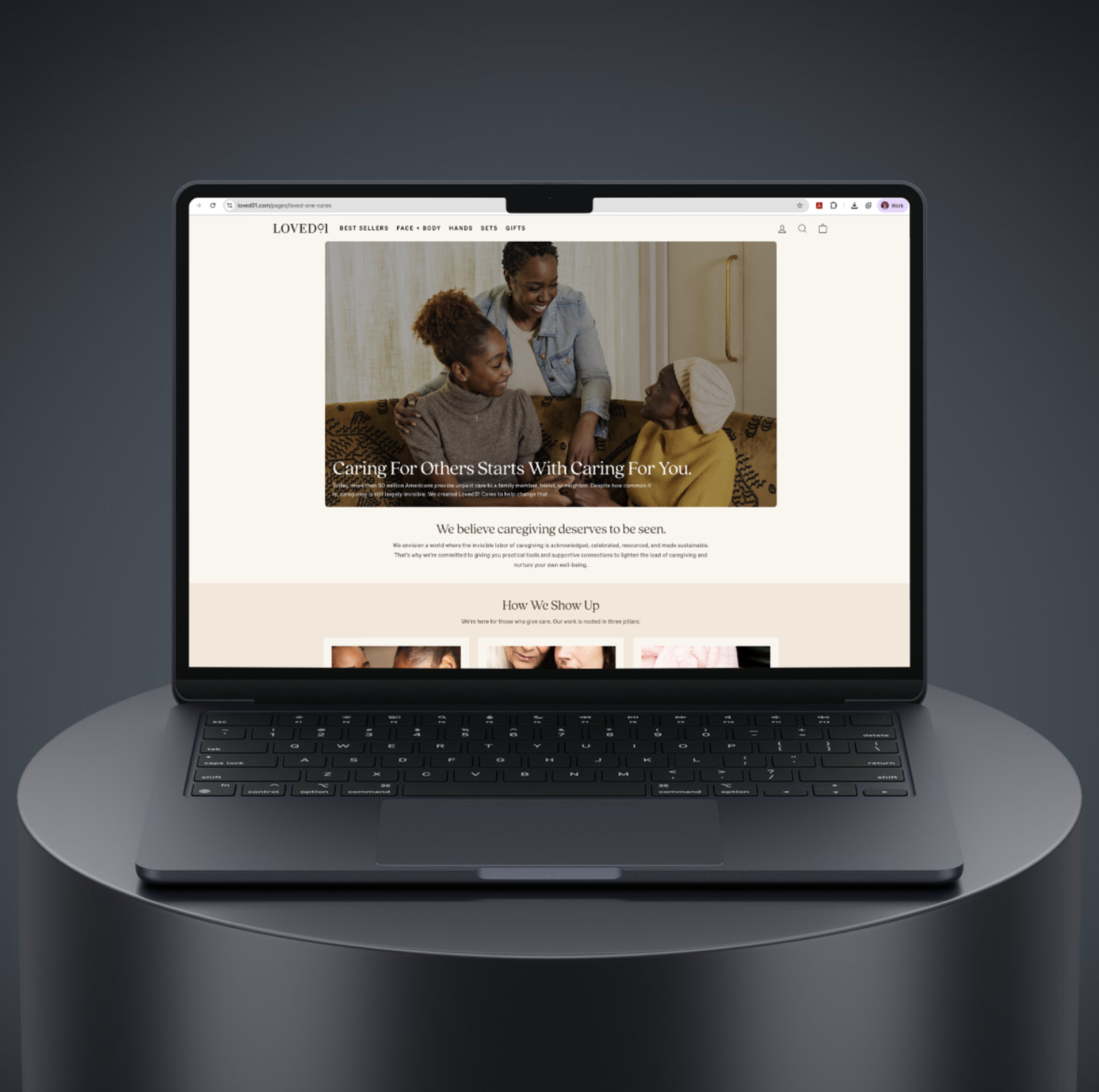 A sleek, black laptop displaying a website about caregiving, with a header menu and a warm, inviting picture of a caregiver with two elderly women.