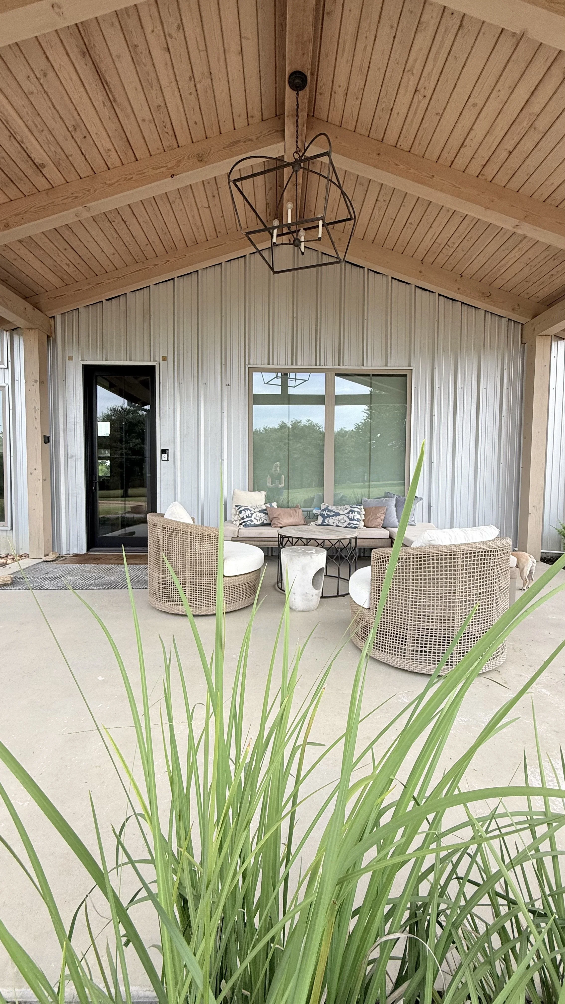 Outdoor patio area with white cushioned seating, a round marble table, and a view of a grassy field with trees and a small playground structure in the distance.