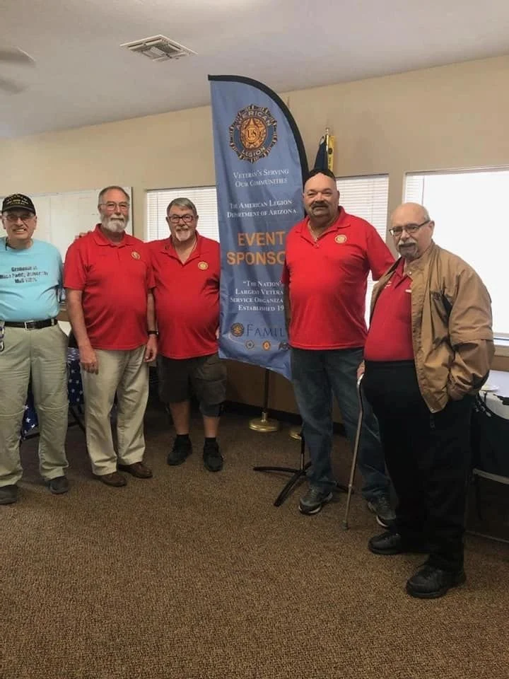 Five men standing inside a room near a Veterans of Foreign Wars banner, with some smiling at the camera.