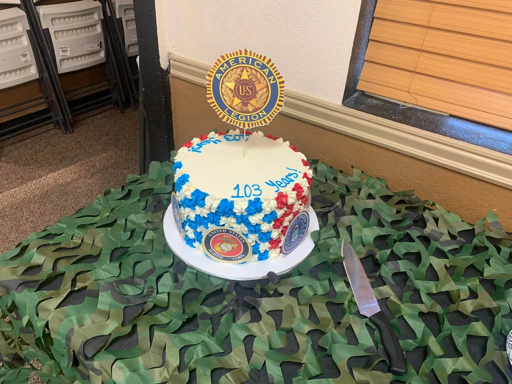 Cake decorated with the United States Marine Corps emblem and a sign that says "103 Years!" surrounded by green camouflage paper.