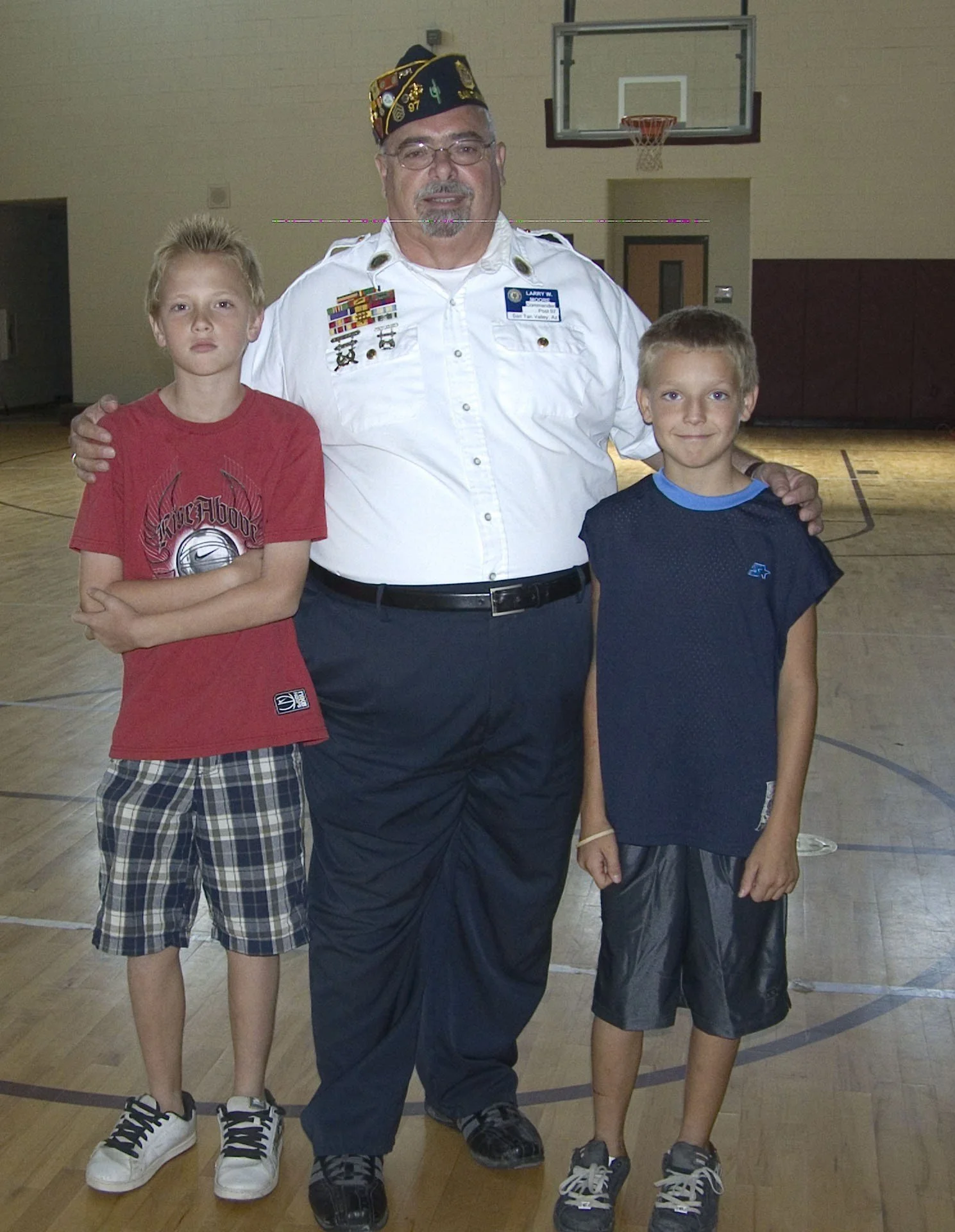 A man dressed in a military uniform standing with two young boys in a gymnasium.