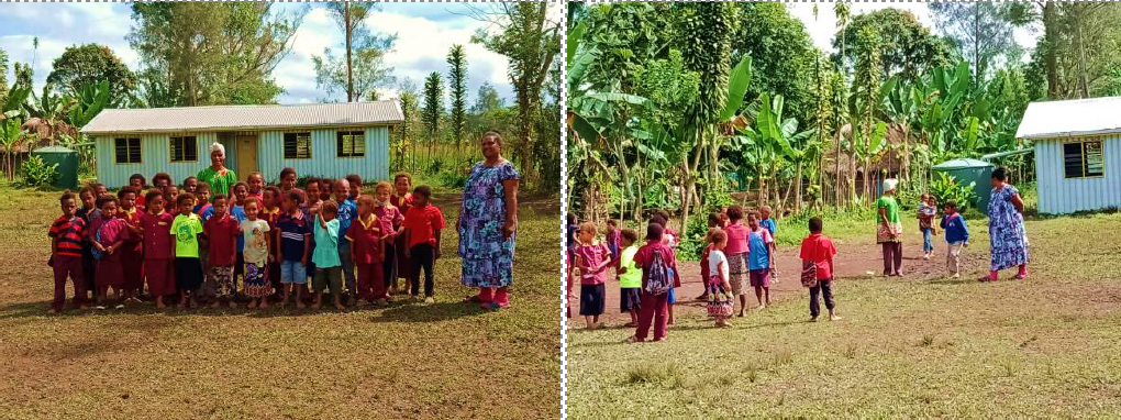 Children and teachers gathered outside a rural school building surrounded by tropical greenery.