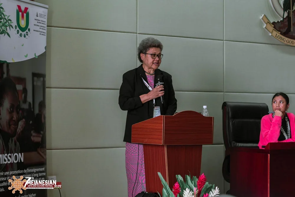 Woman speaking into a microphone at a podium during the Melanesian Arts and Culture Festival 2023
