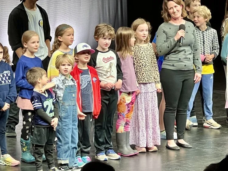 Odyssey Talent Show : Group of children and a smiling woman holding a microphone on a stage