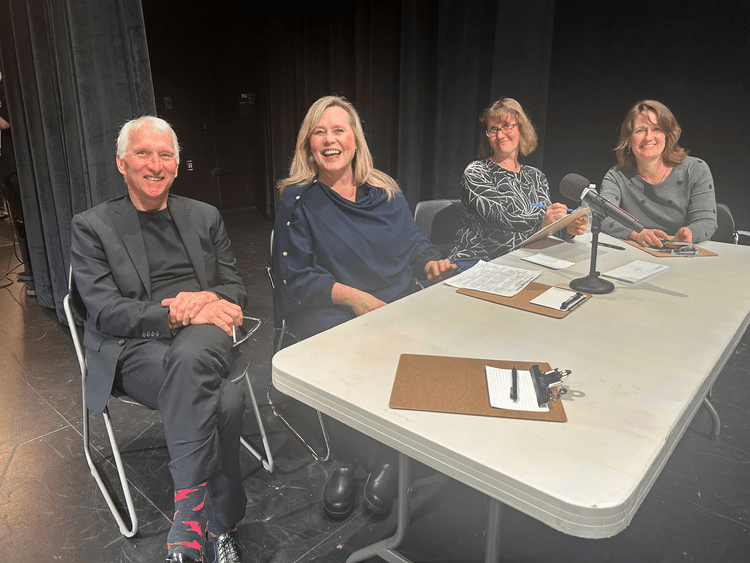 Odyssey Talent Show :  Four adults seated at a panel discussion table on a theater stage with microphones, papers, and clipboards.