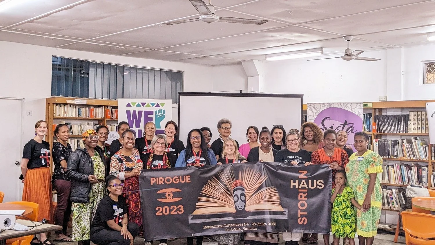 Group photo of diverse women holding a Pirogue 2023 literary festival banner in a library