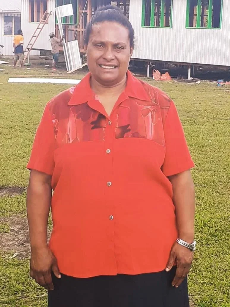 Smiling woman in a red button-up shirt standing on a grassy lawn outside a building under construction
