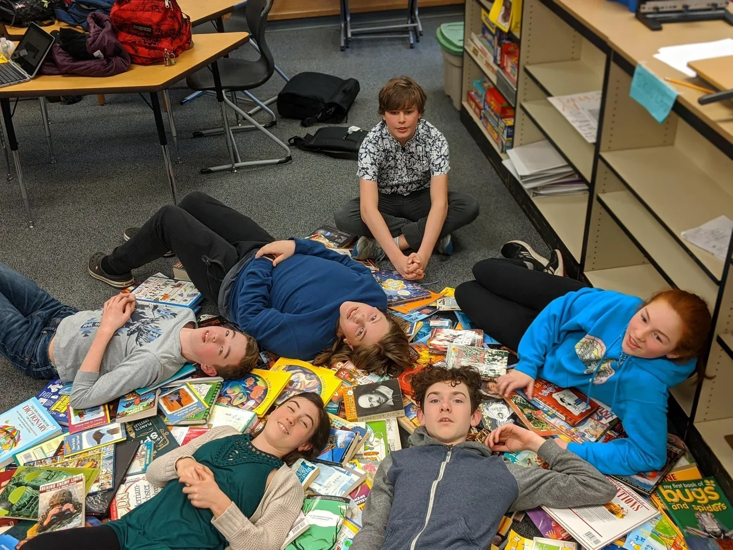 Group of students lying and sitting among scattered books on a classroom floor
