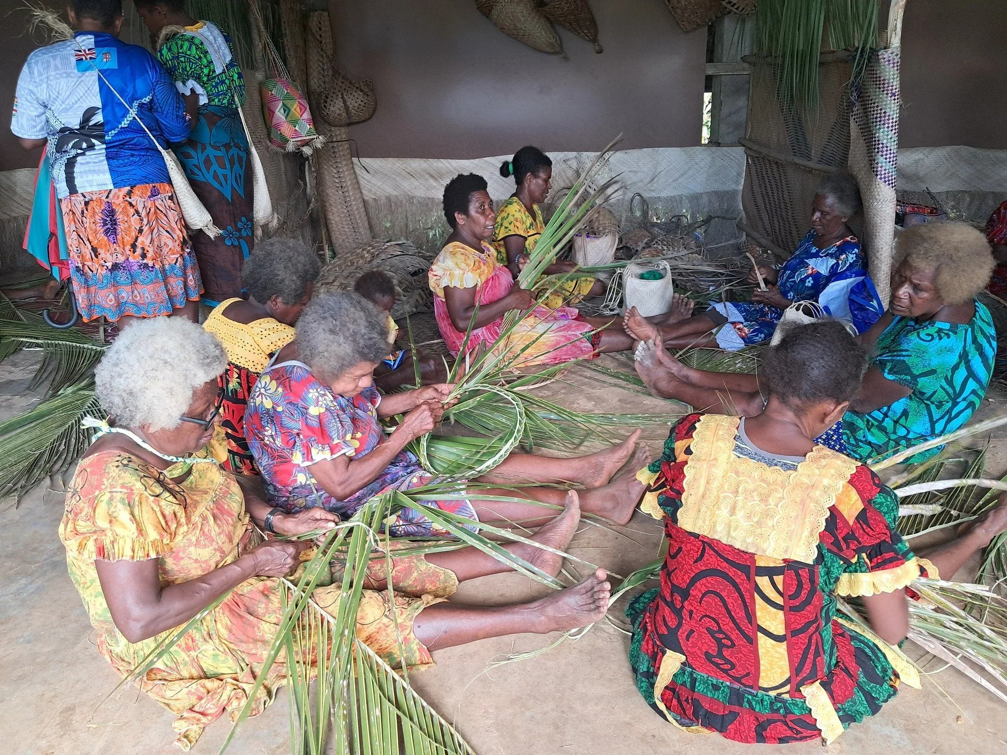 Vanuatu Women weaving baskets and mats from palm leaves inside a traditional Pacific Island house