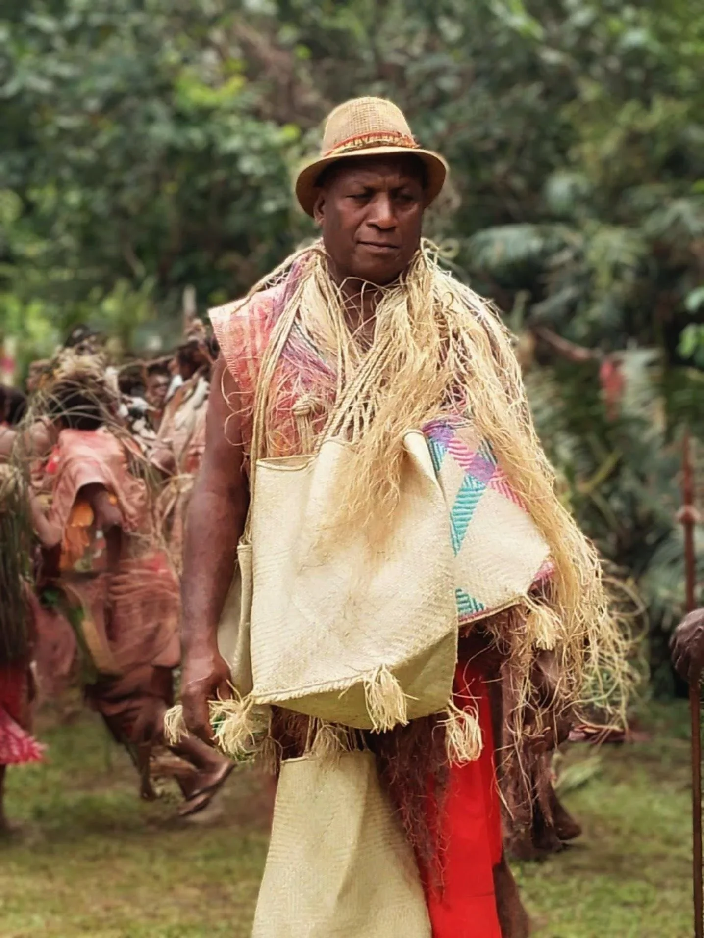 Vanuatu Man in a straw hat and raffia costume standing with traditionally dressed performers in a forest