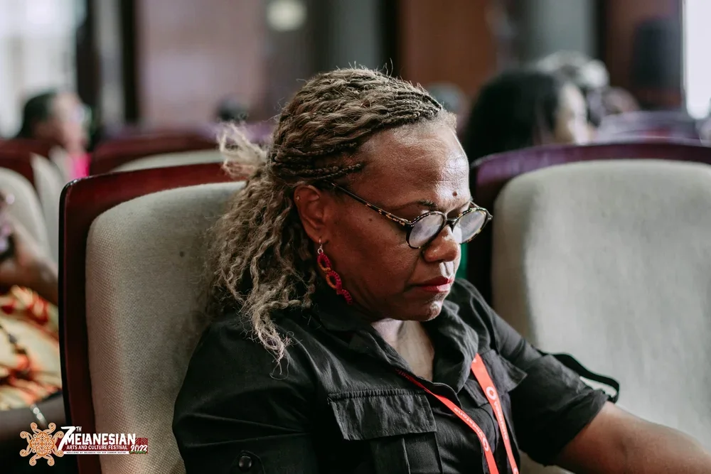 Woman with braided hair and glasses seated at the Melanesian Arts and Culture Festival.
