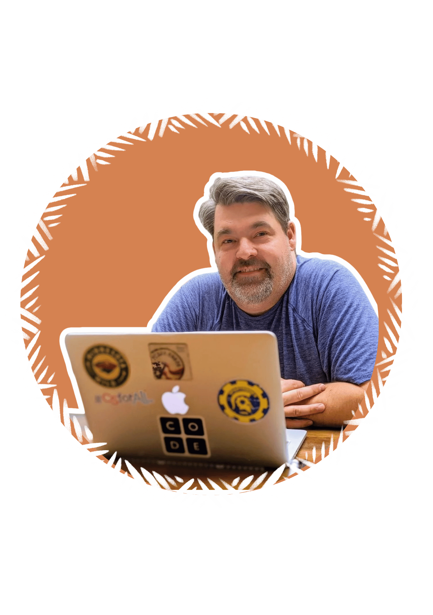 A man with gray hair and a beard, wearing a blue shirt, sitting at a table in front of a silver laptop with various stickers, smiling at the camera. The background features a decorative circle with white lines and a brown and black design.