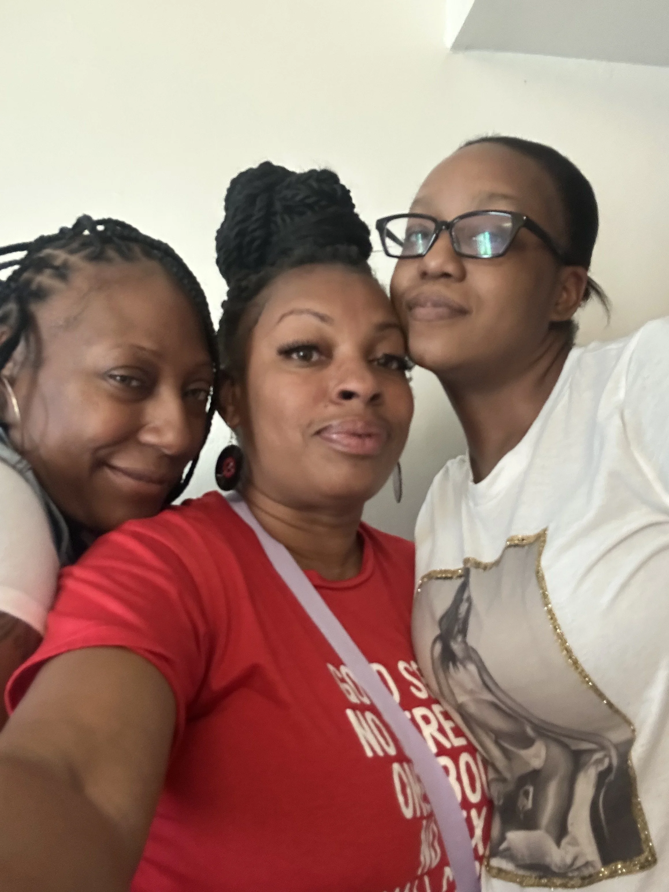 Three women taking a selfie together, smiling, with light-colored walls in the background.
