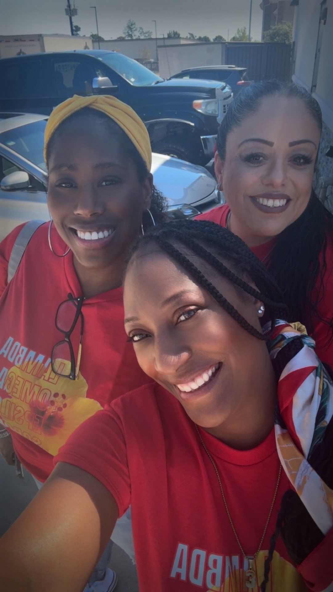 Three women taking a selfie in a parking lot, all wearing red shirts, smiling at the camera.