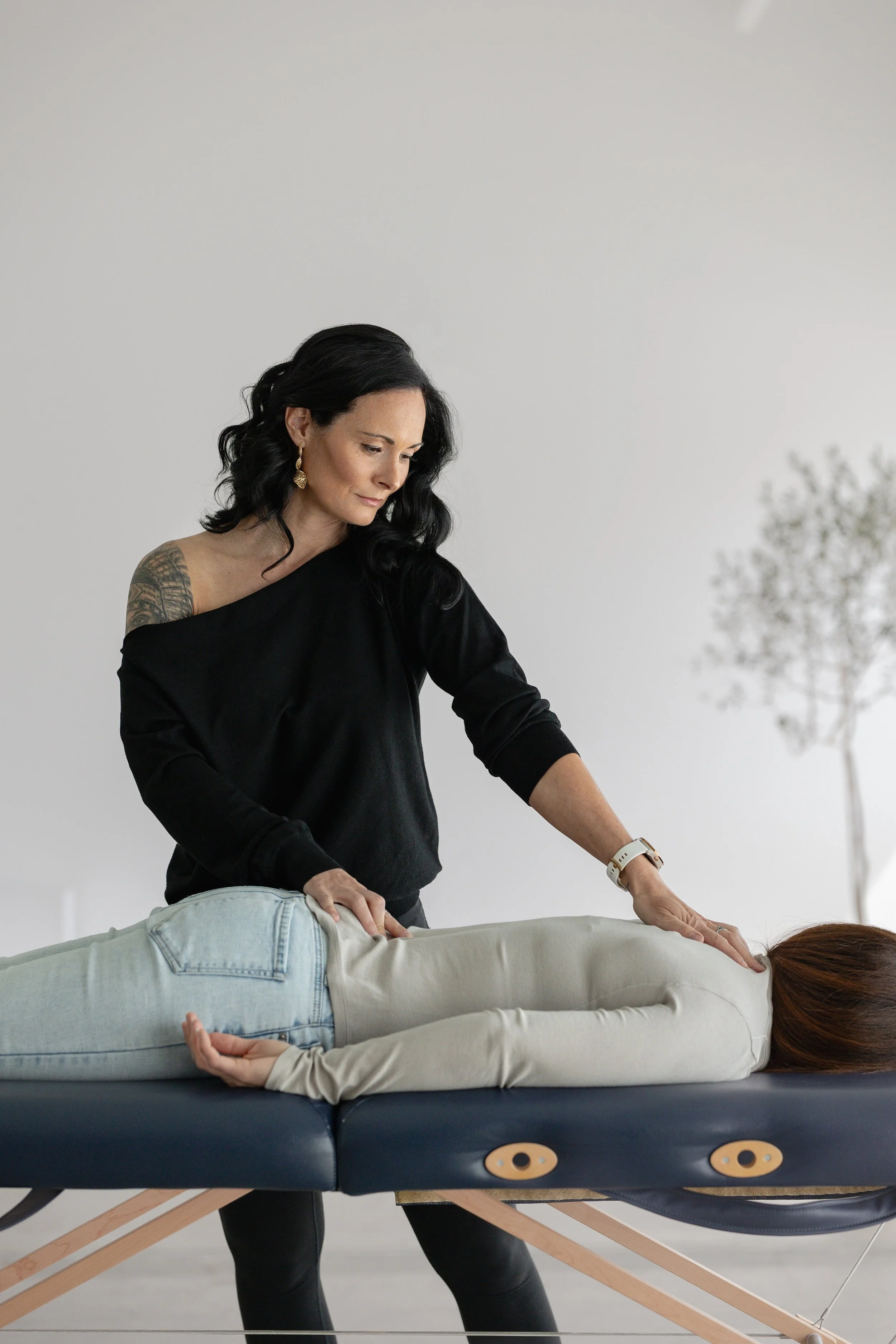 Une thérapeute pratique une séance de massage ou de thérapie de manipulation sur un patient allongé face contre terre sur une table de massage dans une pièce minimaliste.