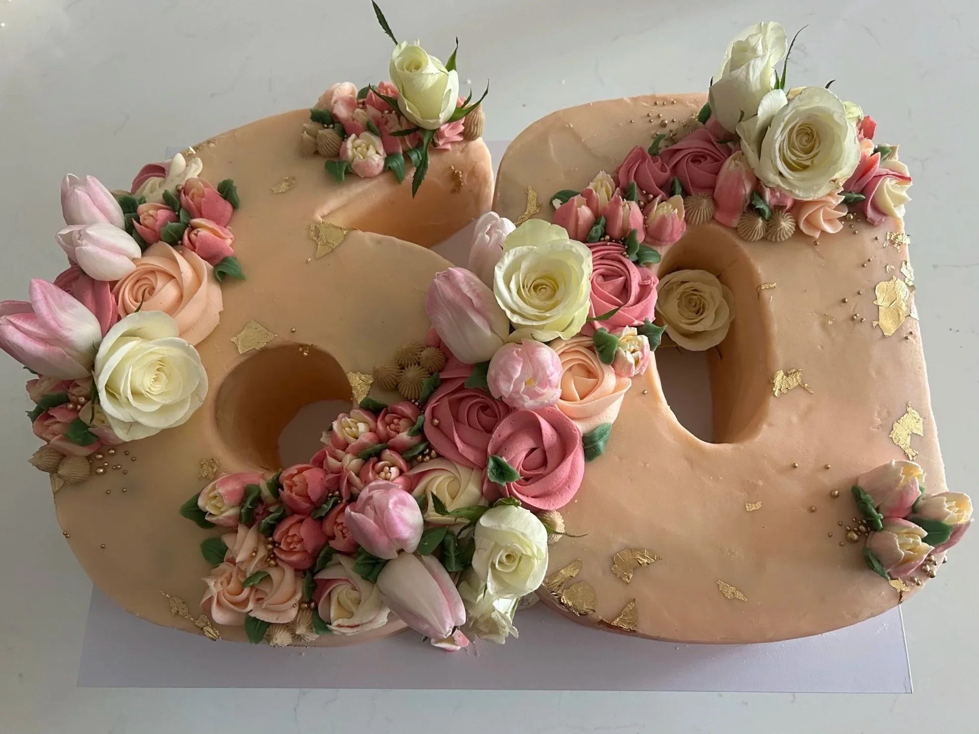 Decorative cake with pink, peach, and white roses, tulips, and gold leaf accents.