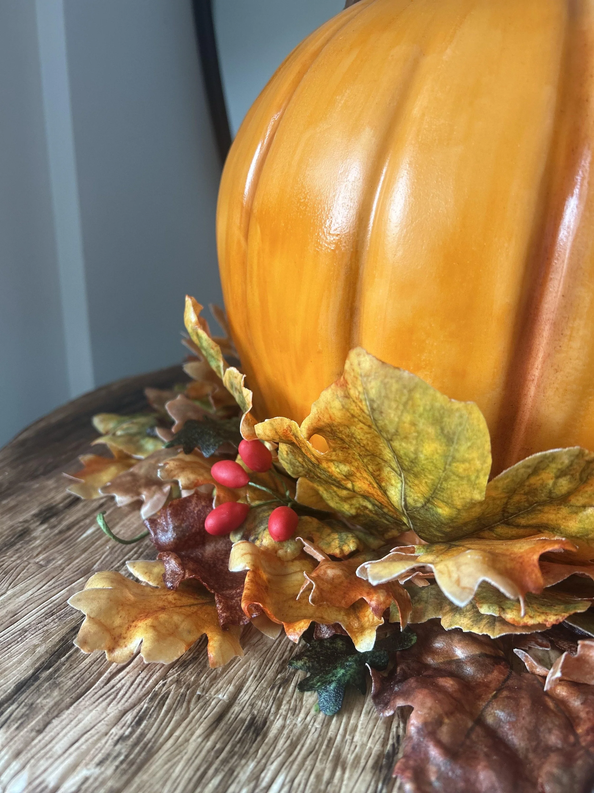 Close-up of a pumpkin surrounded by autumn leaves and red berries, placed on a wooden surface.