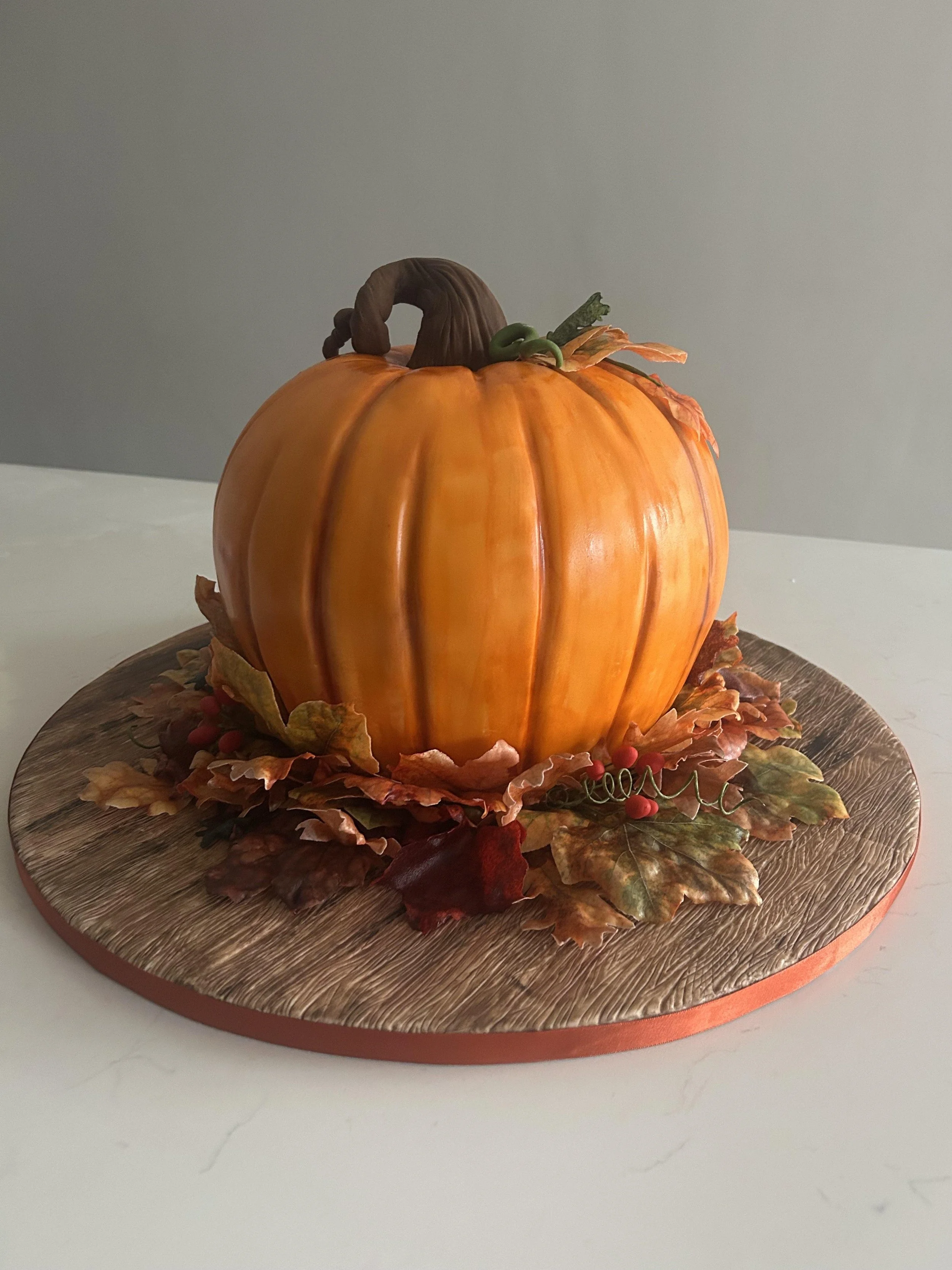 Decorative pumpkin centerpiece with artificial fall leaves and berries on a wooden circular tray.