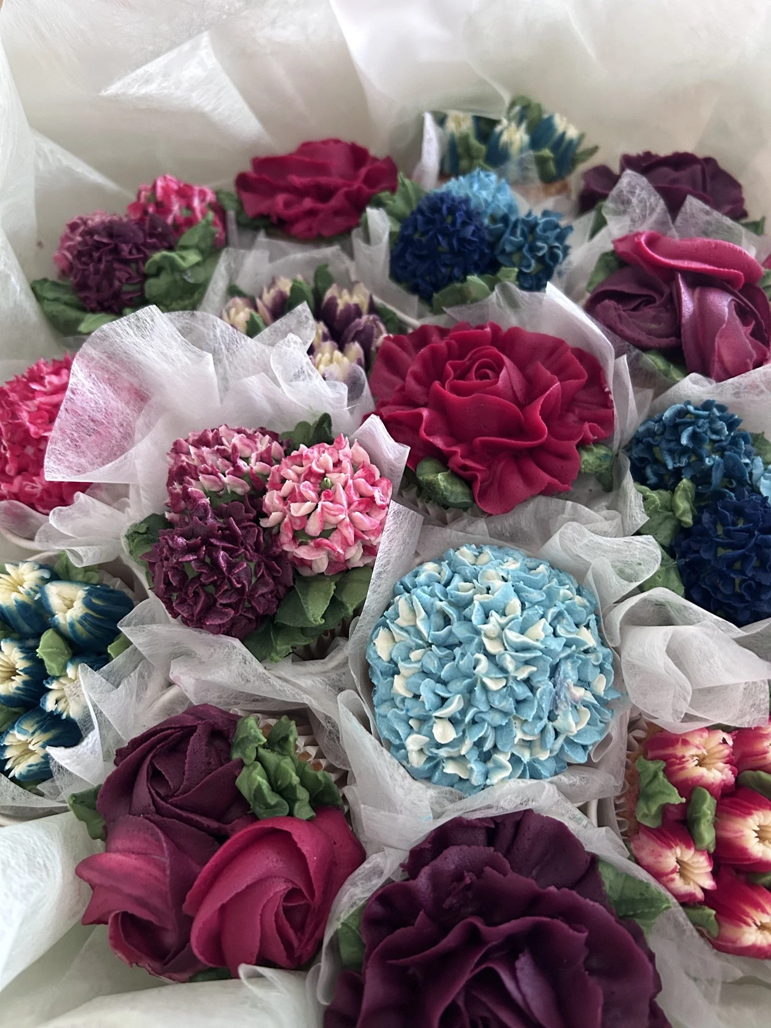 Bouquet of colorful artificial flowers including roses, hydrangeas, and other blossoms wrapped in white tissue paper.