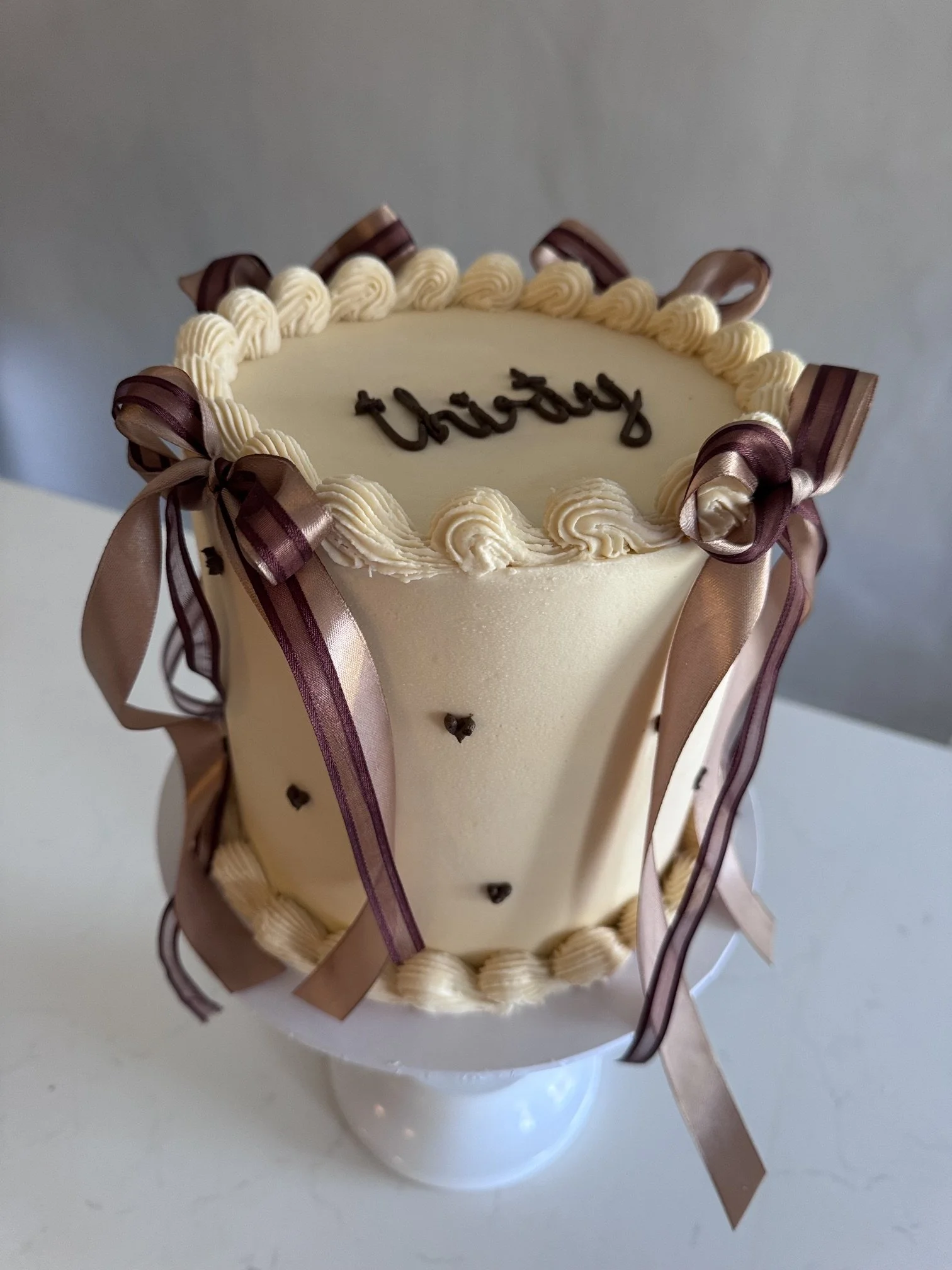 A white birthday cake with white frosting, decorated with chocolate ribbons and the word 'birthday' written in chocolate on top.