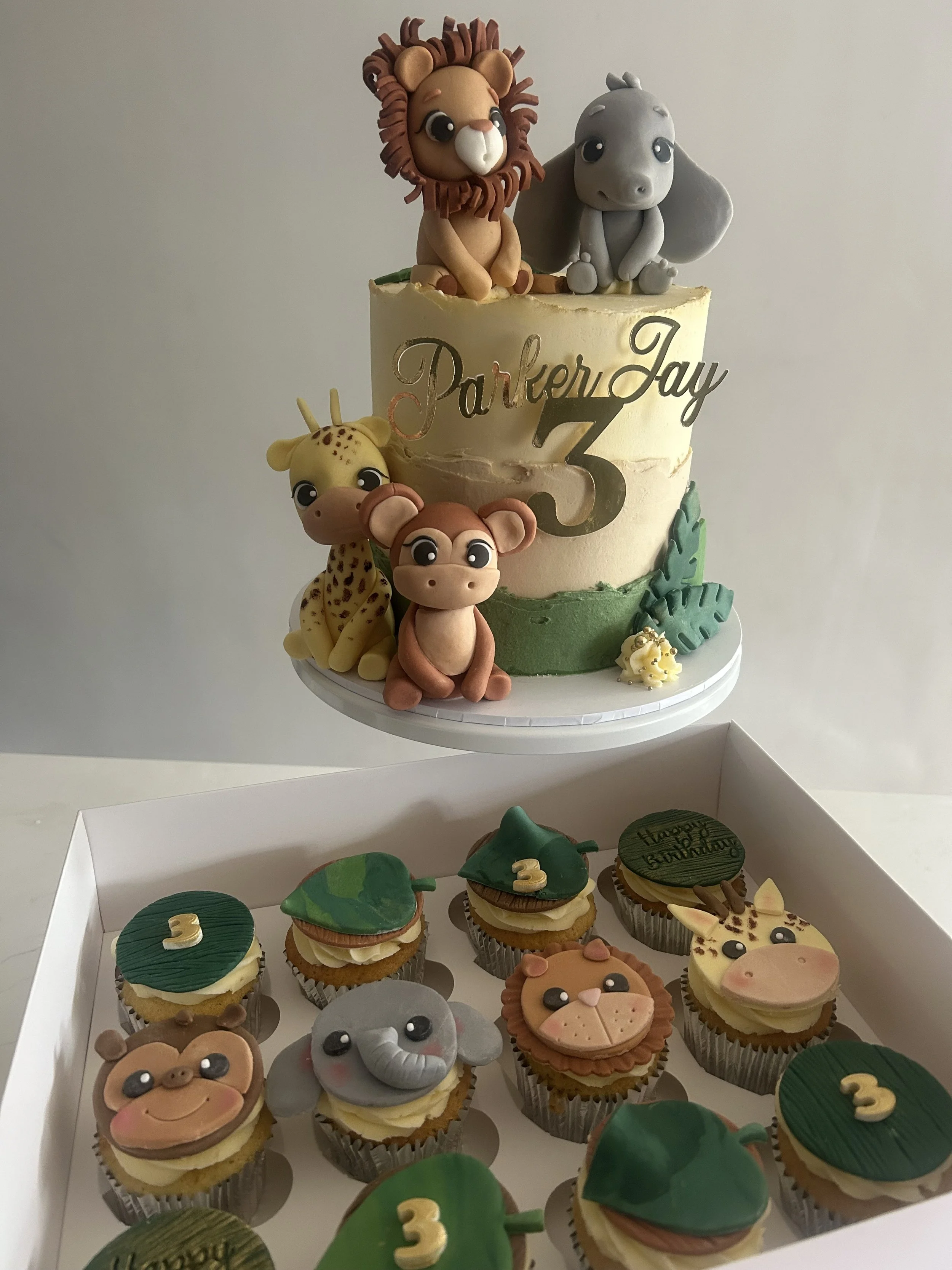 Cupcakes decorated with jungle animal theme, featuring animals such as a lion, elephant, giraffe, and monkey, with some cupcakes decorated with leaves and a birthday message for Parker Jay's 3rd birthday.