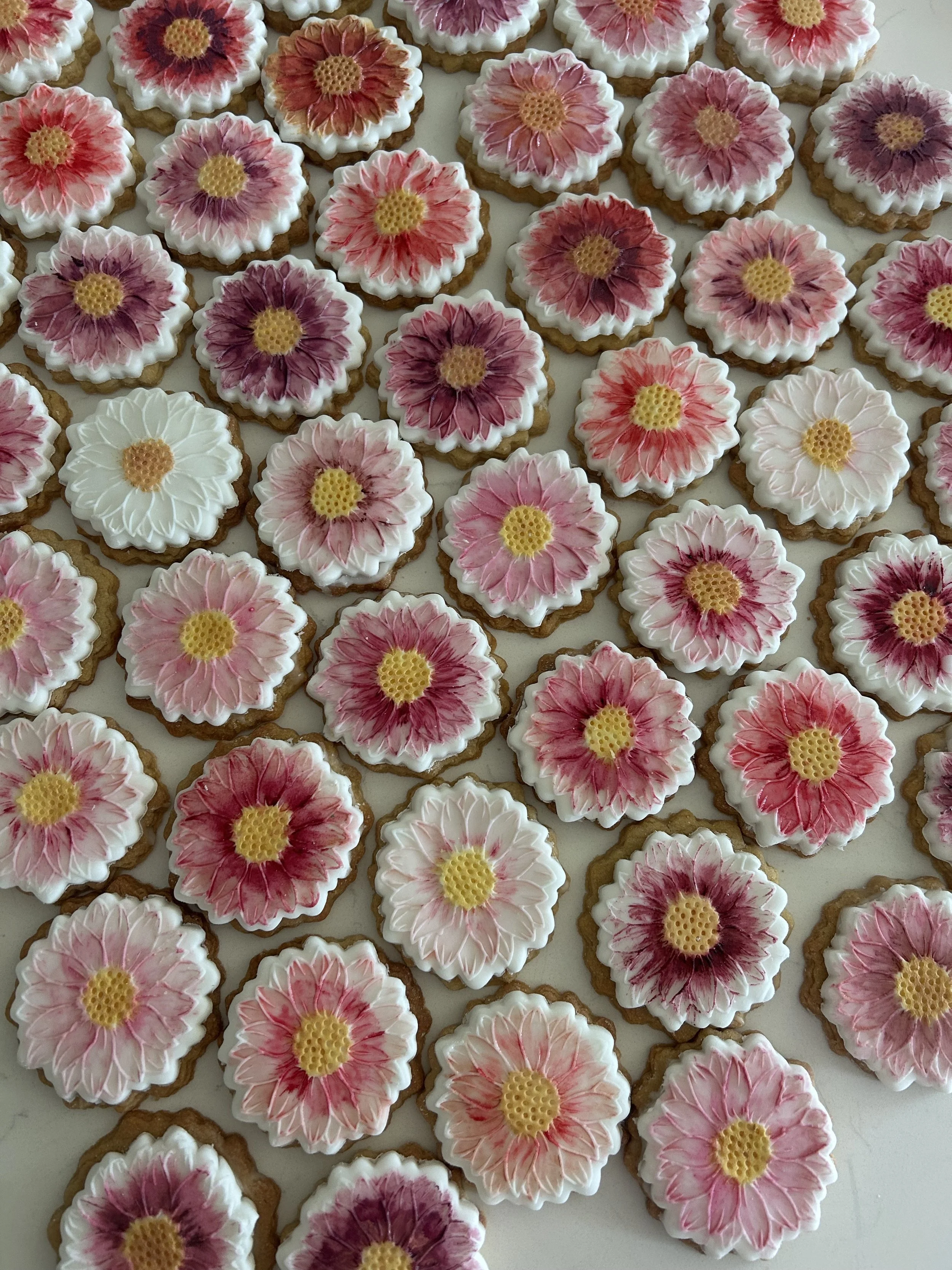 Assorted flower-shaped cookies with pink and white icing, arranged on a white surface.