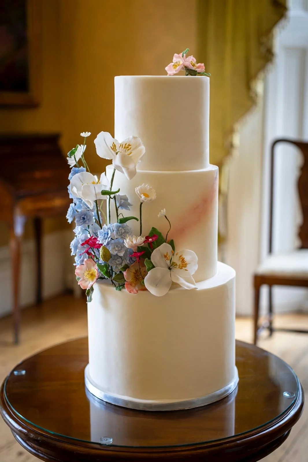Elegant three-tier white wedding cake decorated with fresh pink and white flowers.