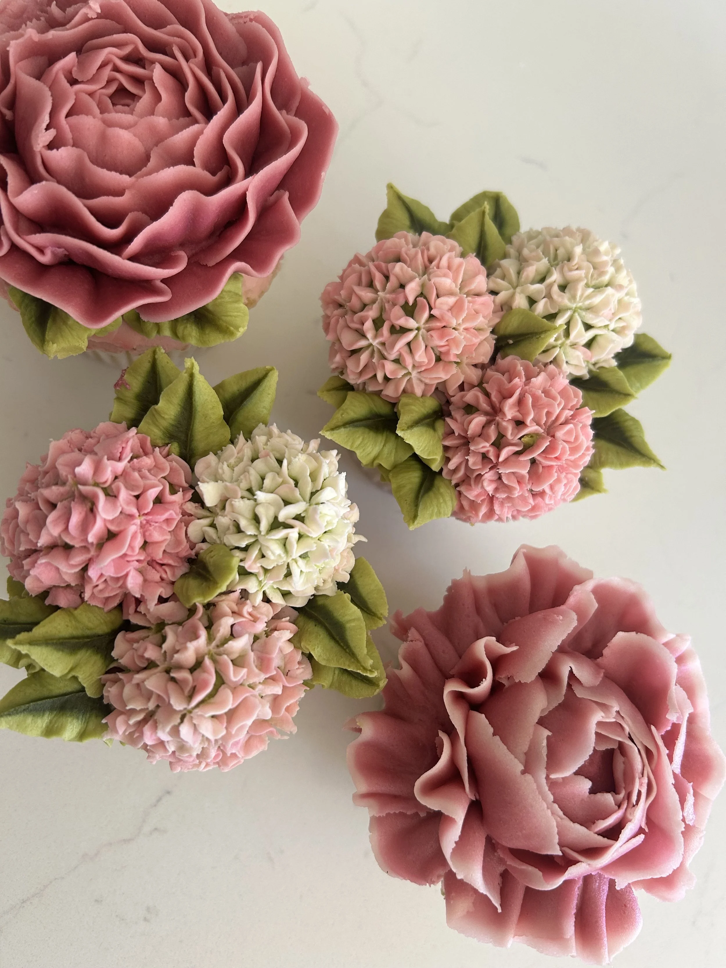Decorative flowers made of pink and white frosting with green leaves, arranged on a white surface.