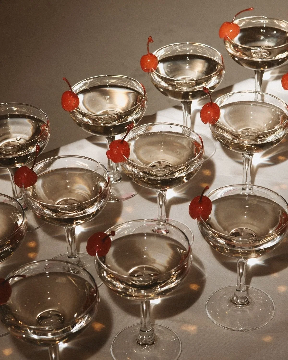 Multiple empty cocktail glasses with red cherries on the rim, arranged on a white surface.
