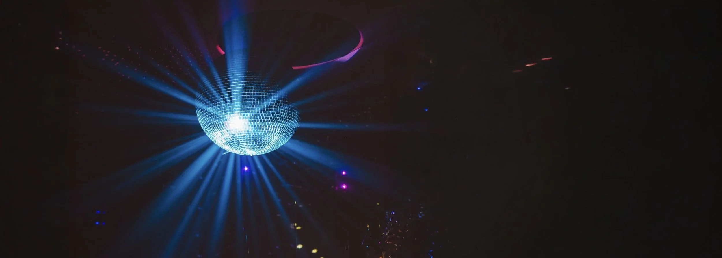 A disco ball emitting blue and purple light beams in a dark setting.