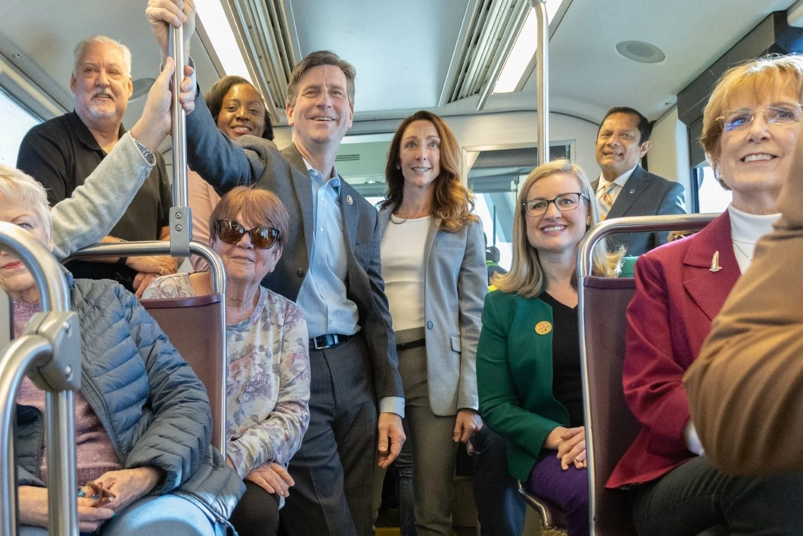 A group of diverse people sitting and standing on a bus, smiling and posing for a photo.