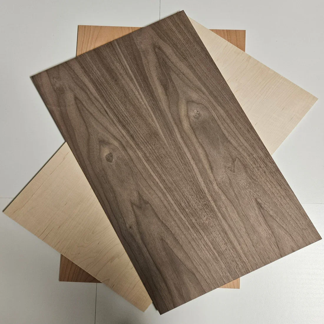 Three samples of wood veneer sheets with different wood grain patterns and colors layered on top of each other.