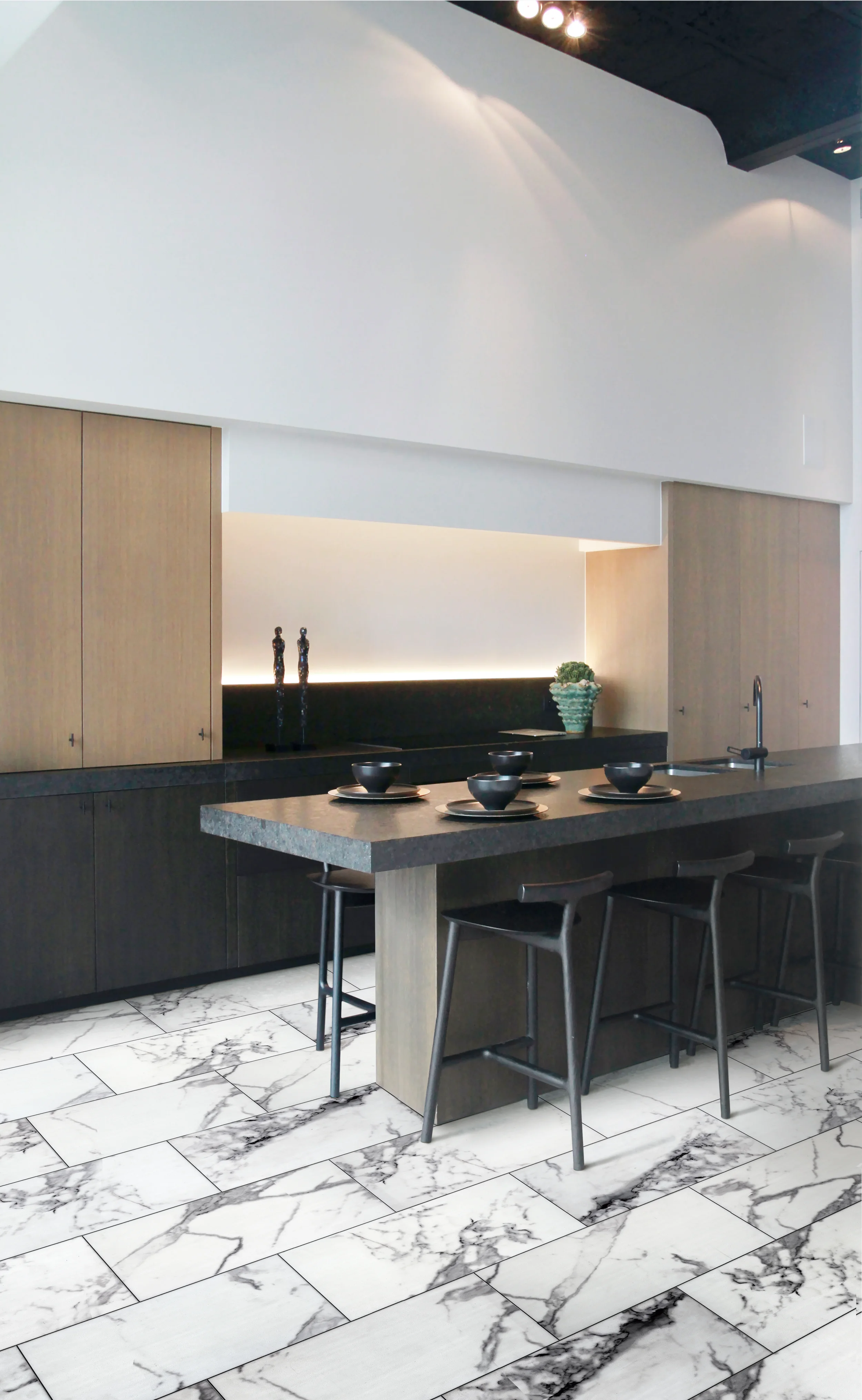 Modern kitchen with marble floor, black and wood cabinets, and a black marble countertop with four black bowls and four black chairs at the counter. Two tall decorative sculptures and a plant are on the backsplash ledge, with a white wall and ceiling in the background.