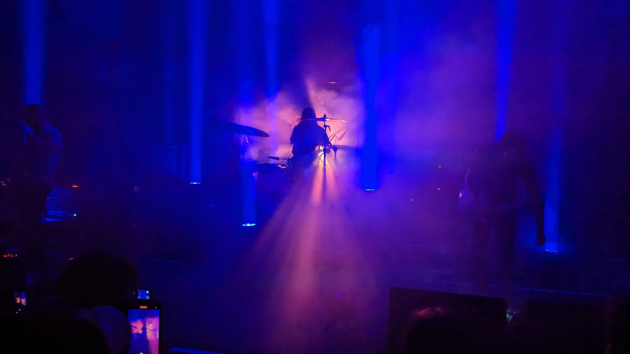 Live music in full force — a band onstage in blue and purple light and haze, the crowd close in the dark.