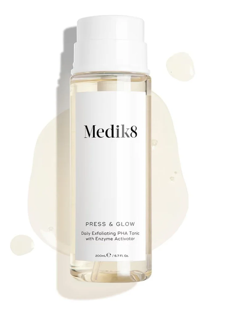A clear bottle of Medik8 skincare toner with a white cap, labeled 'Press & Glow', against a white background with liquid splashes.