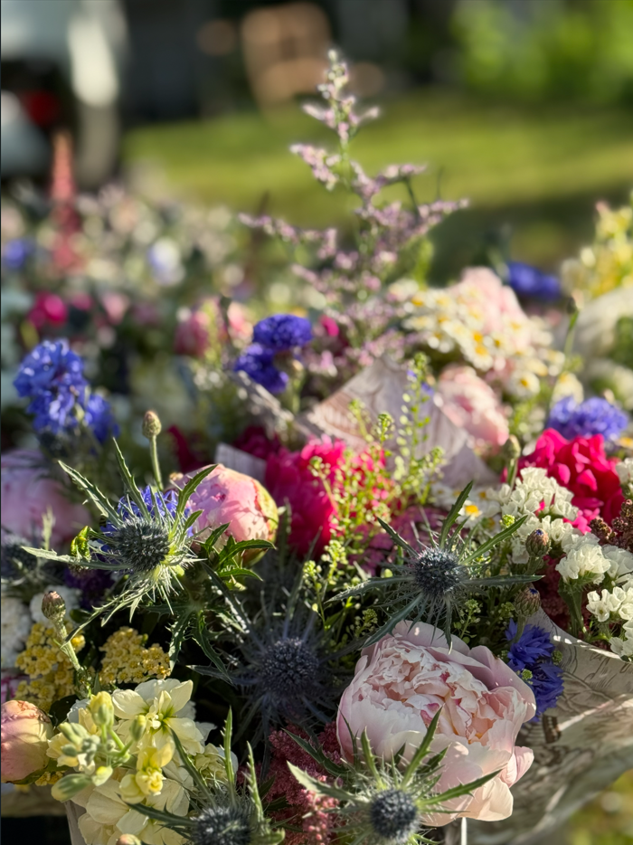 Colorful bouquet of flowers including pink, purple, white, and yellow blossoms with greenery, displayed outdoors.
