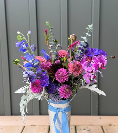 A bouquet of pink, purple, and blue flowers in a blue and white ribboned vase.