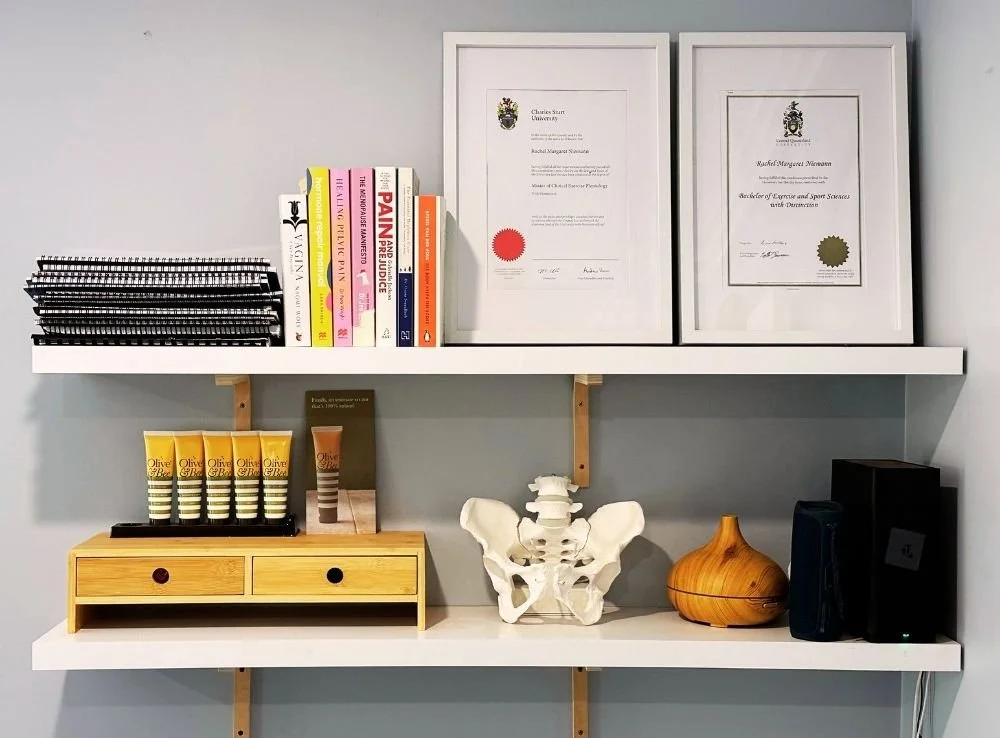 Shelves in Ebb & Flow Exercise Physiology clinic showing pelvic health related items including books, lubricant and a model pelvis