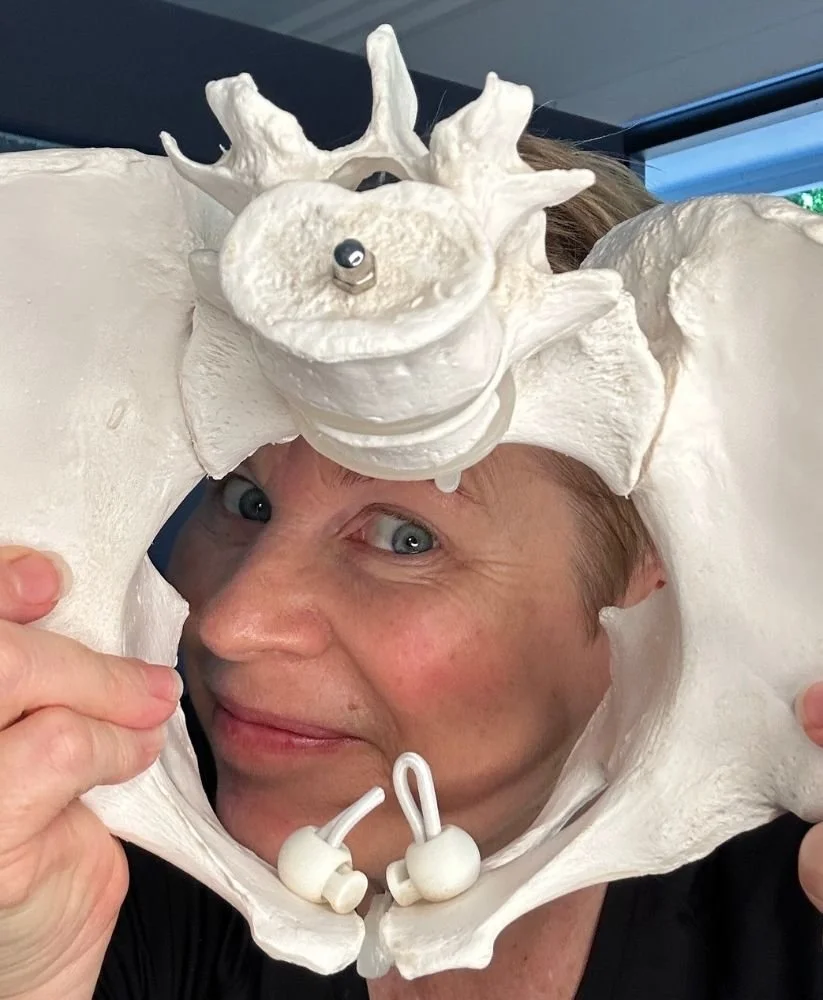 Rachel holding a model pelvis up to her face and looking through it with a cheeky grin