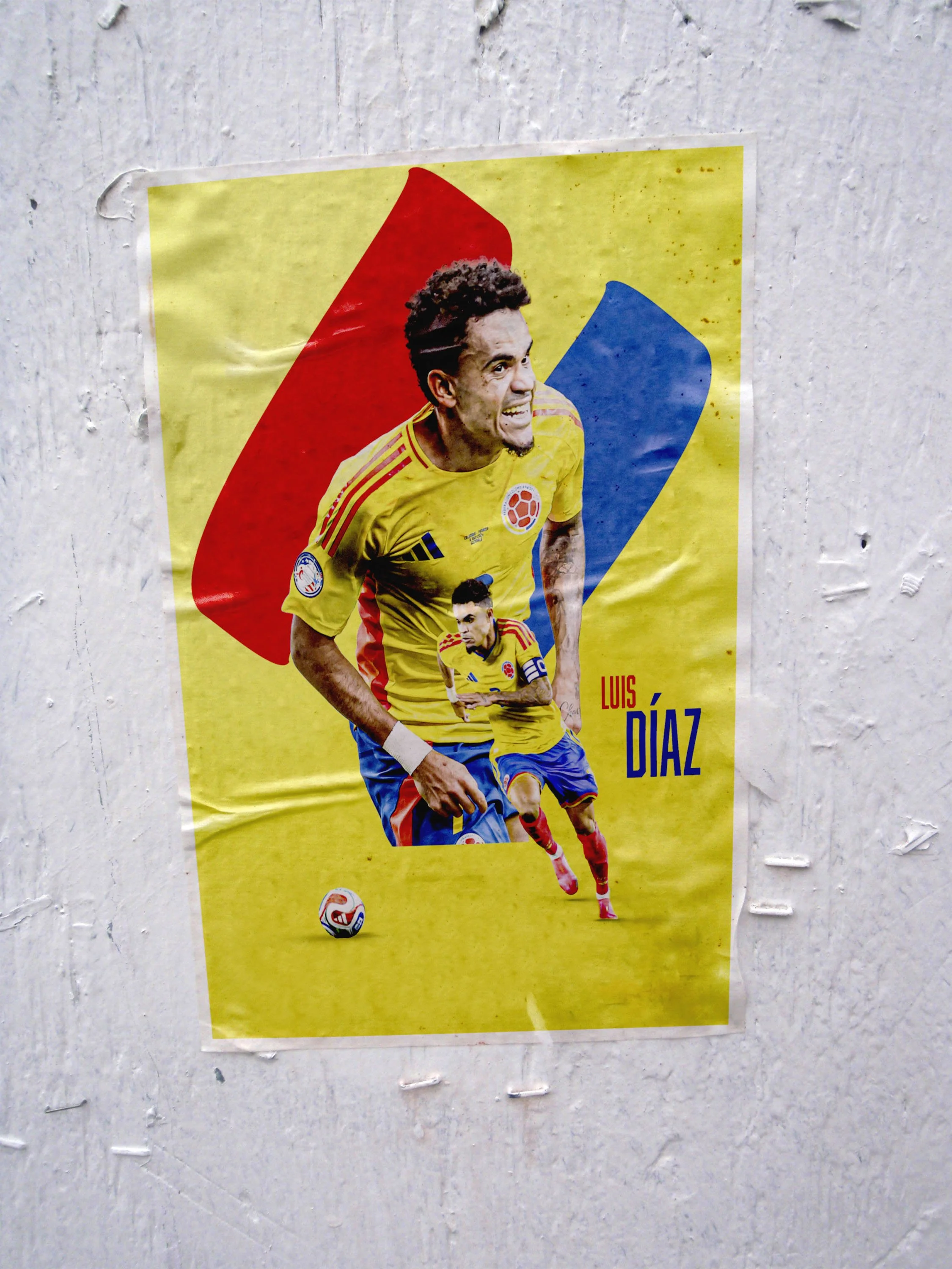 Poster of a Colombian soccer player in a yellow jersey dribbling a soccer ball, with his name Luis Díaz written on the poster, set against a yellow background with red, blue, and yellow abstract shapes.
