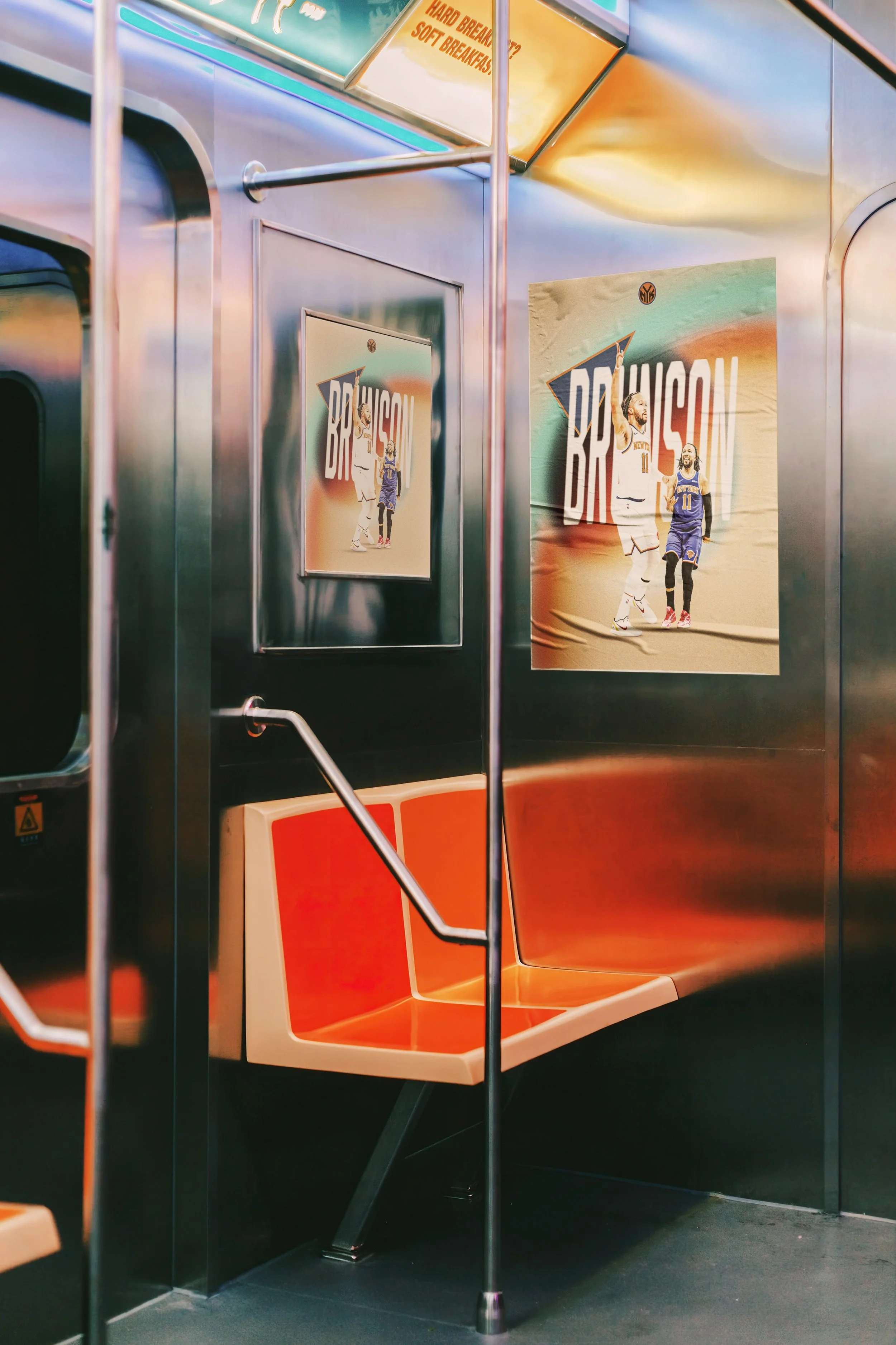 Inside a subway train with orange and beige seats, metal poles, and advertisements on the wall, including a sports poster featuring two basketball players.