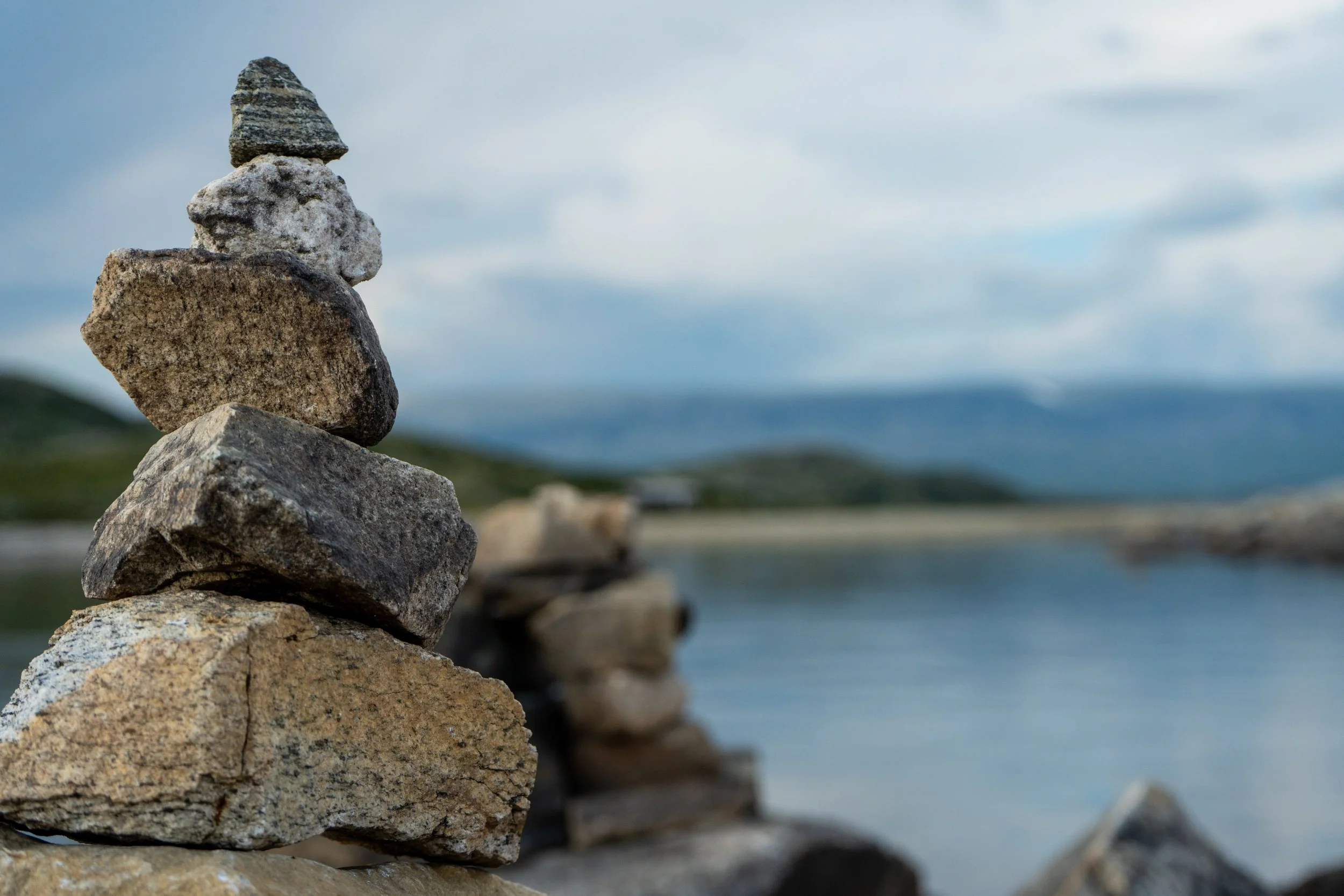 A stack of several irregularly shaped rocks in the foreground with a blurred background showing the sky and water.