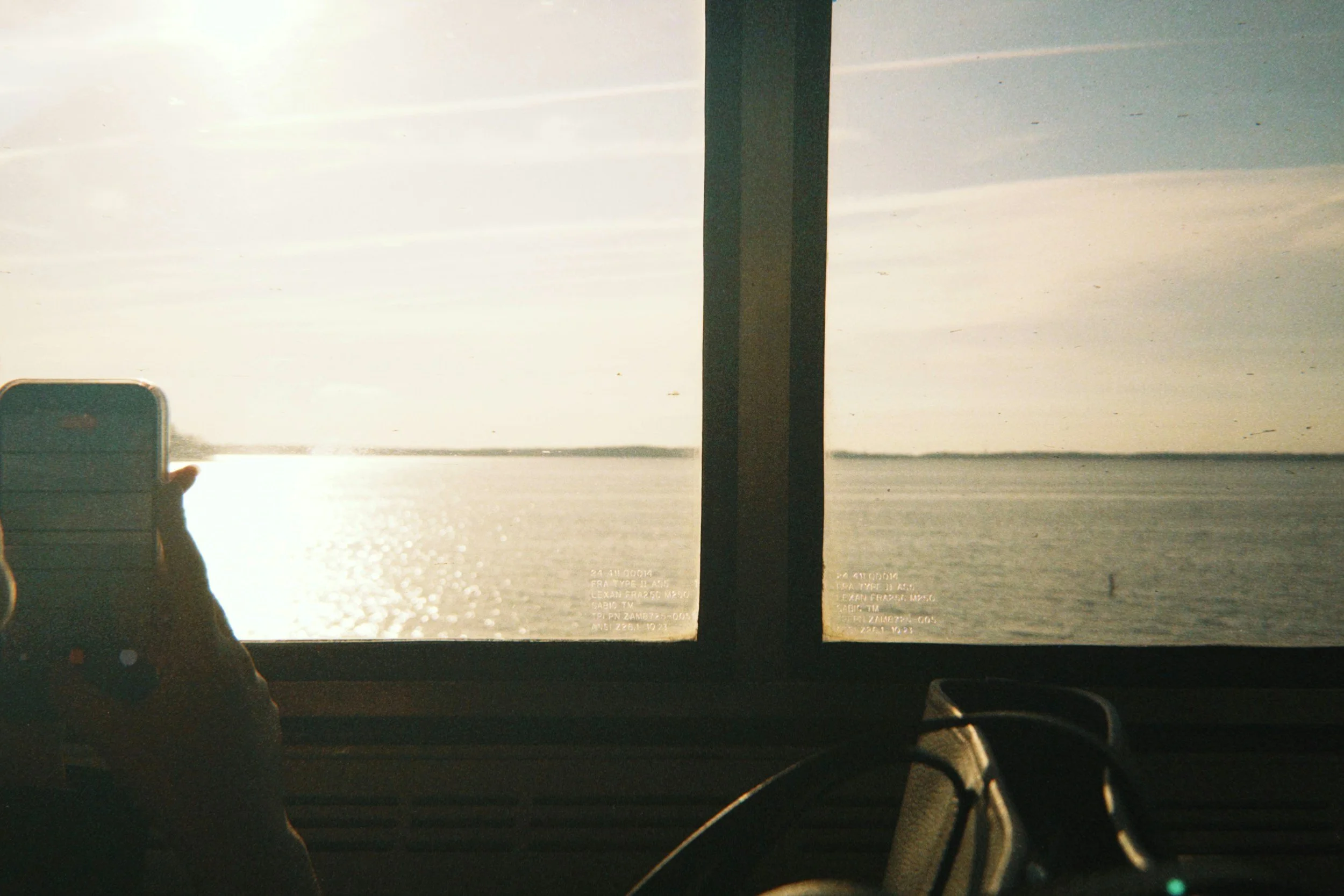 Photograph of a beach scene viewed through a camera's viewfinder, showing the ocean, sky, and a pole in the middle. Part of a person's hand and a suitcase are visible in the bottom left corner.