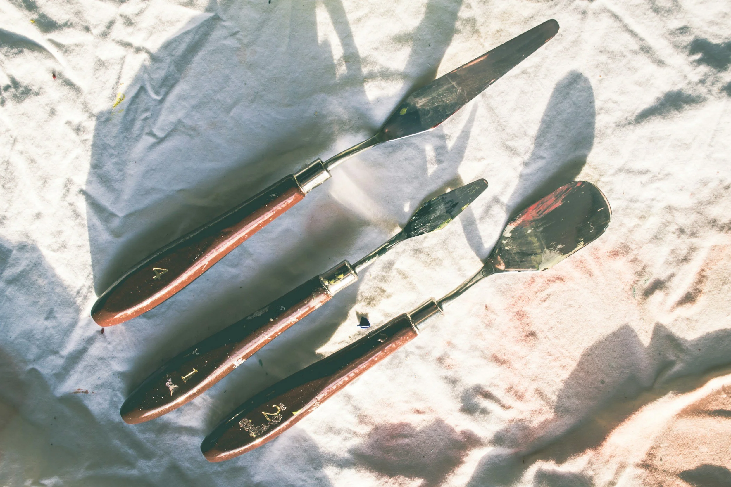 Four gardening tools lie on a white surface: a trowel, a smaller hand trowel, and two small transplanters.