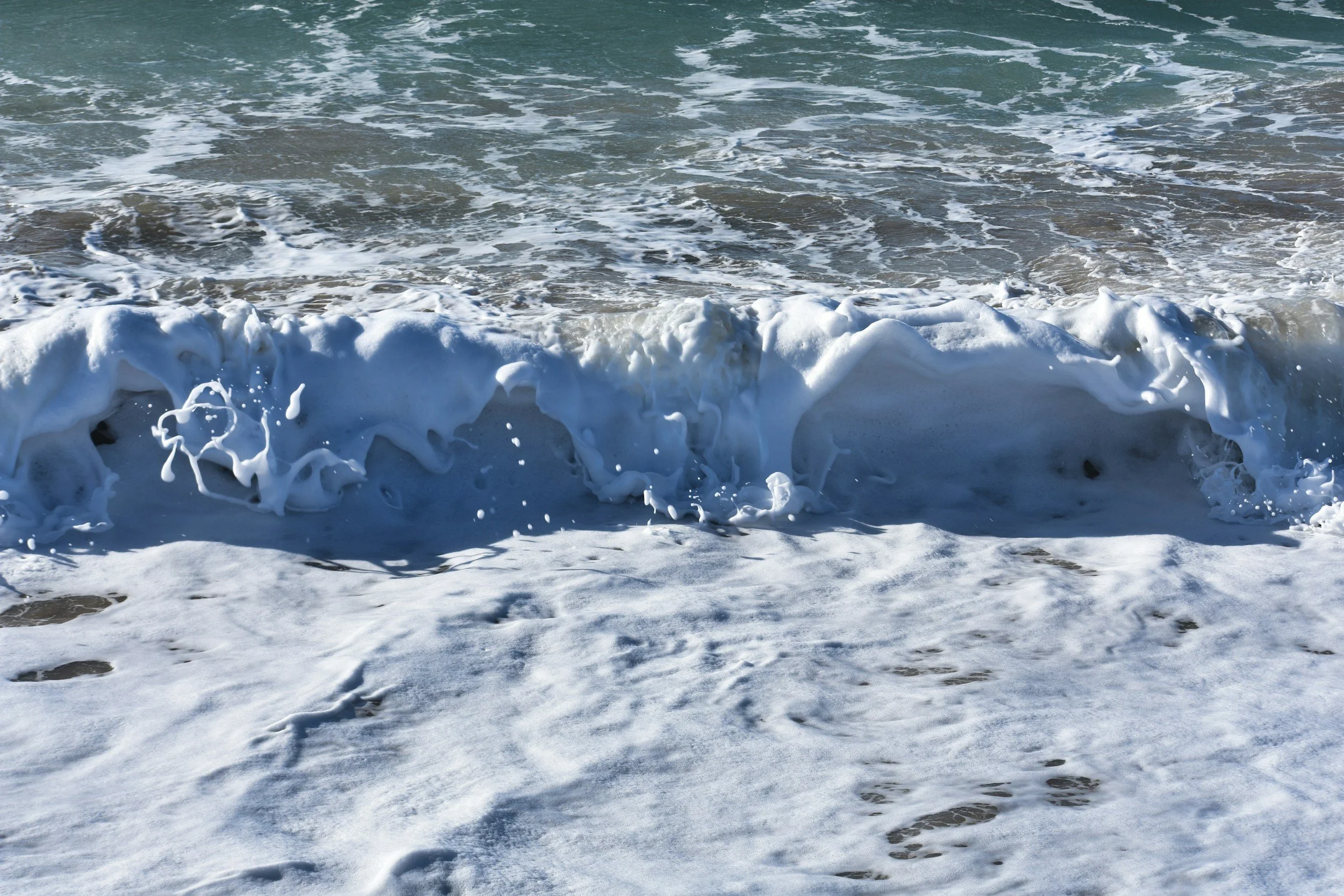 Ocean waves crashing on the sandy shoreline with sea foam and water spray.