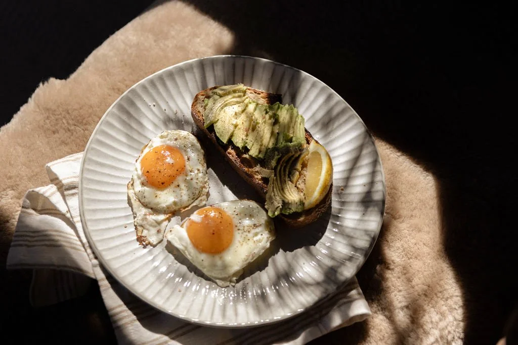 Plate with two sunny-side-up eggs and avocado toast with lemon slices on top