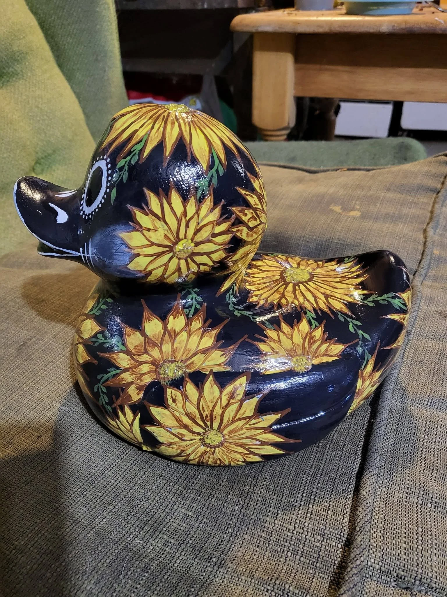 Painted ceramic dog figurine with yellow and orange sunflower pattern on black background, sitting on a textured surface.