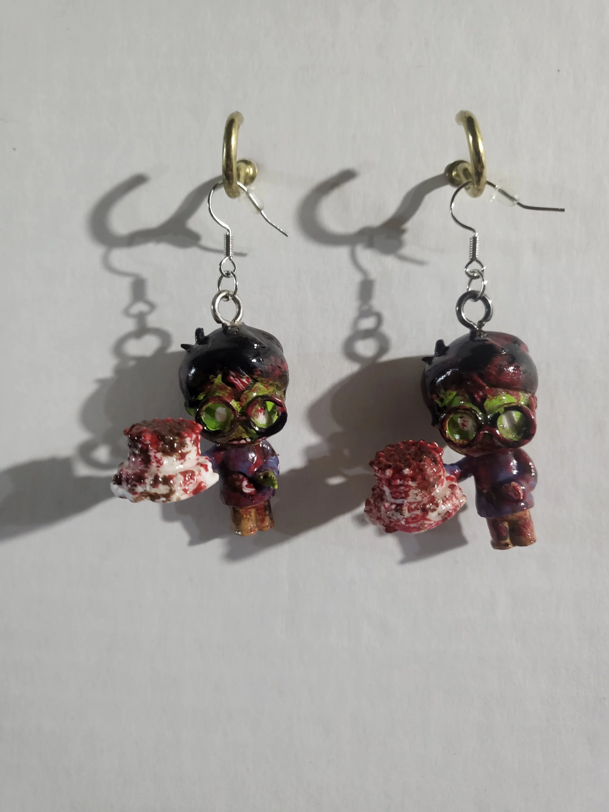 Pair of earrings with colorful, irregularly shaped glass beads hanging from gold hooks against a white background.